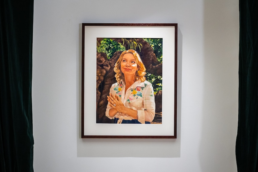 An oil painting of Justine Clarke standing under a tree with light on her face and hair