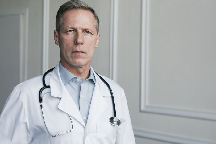 Serious male doctor in a white coat with a stethoscope looking sternly at the camera
