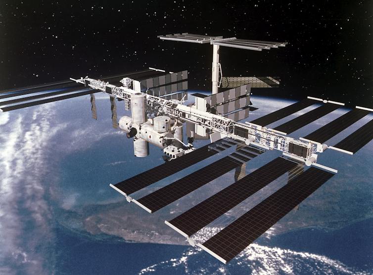 Black solar panels attached to while tubular structures hovering over Earth.
