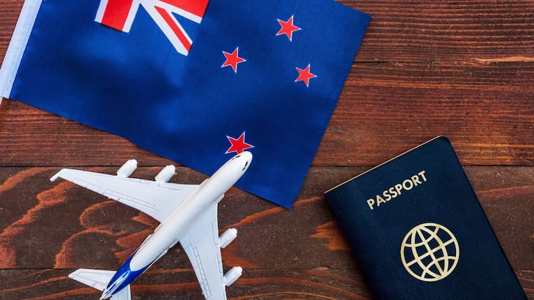 Flag of New Zealand with passport and toy airplane on wooden background.