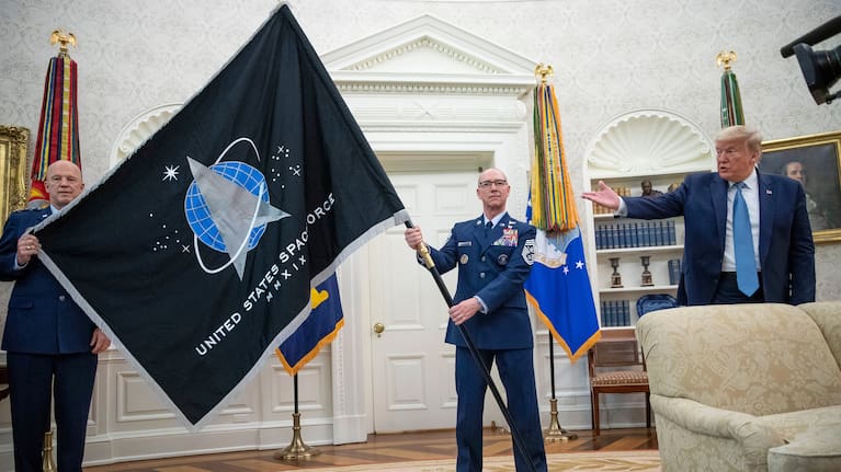 General John "Jay" Raymond, left, and Chief Master Sergeant Roger Towberman, centre, hold the Space Force Flag as President Donald Trump gestures to it at a presentation in the Oval Office.