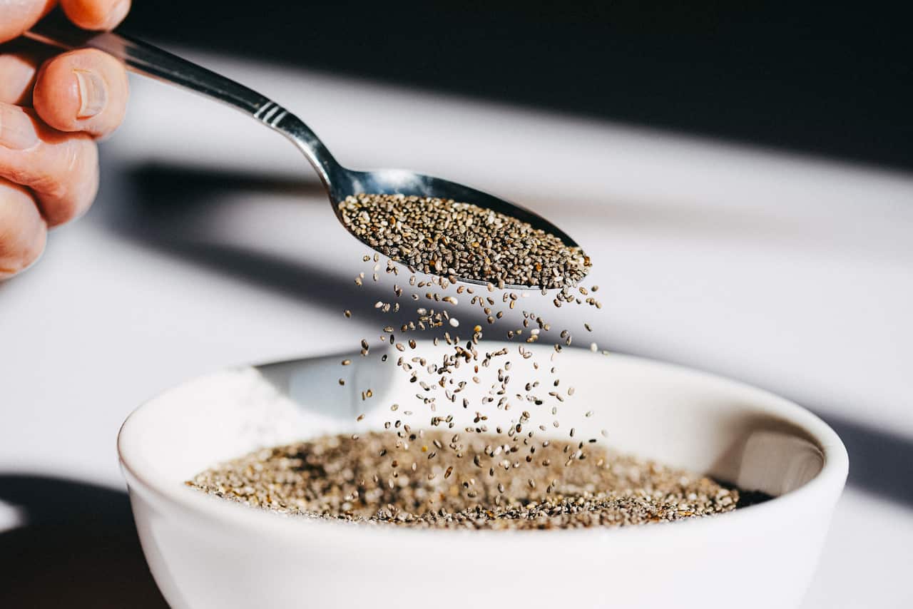 Light shines on a spoon as chia seeds are poured into a white bowl, creating a dynamic motion