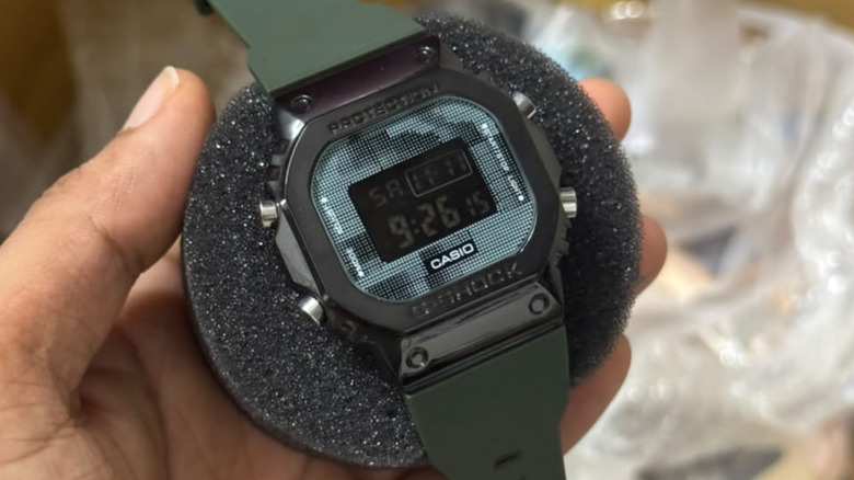 Casio G-Shock digital watch with a green strap held in hand.