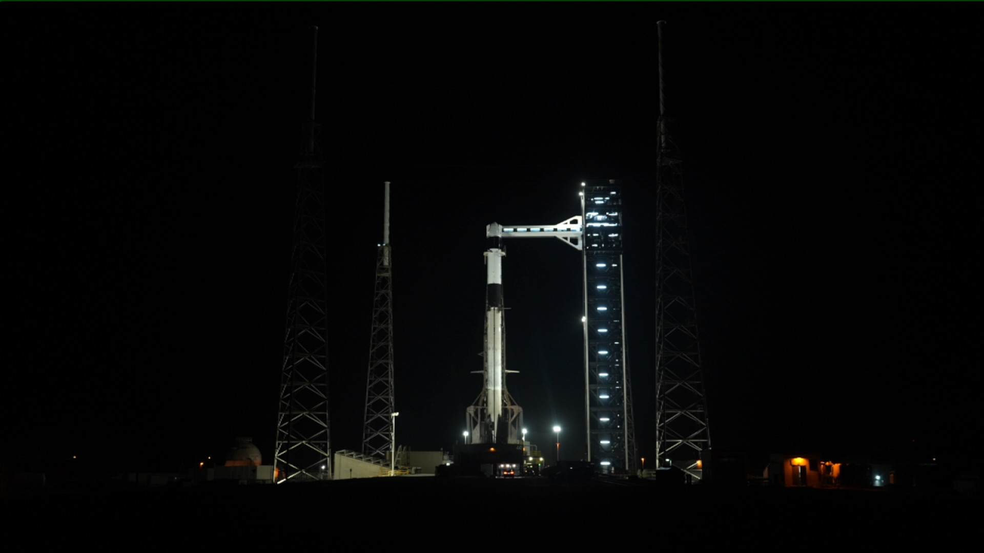 a white and black rocket is seen from afar, sitting on its launch pad at night