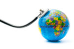 The chestpiece of a stethoscope rests on a miniature globe of the world.