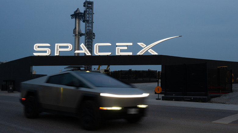 SpaceX facility in half-light with an illuminated SpaceX logo and a Cybertruck in the foreground.