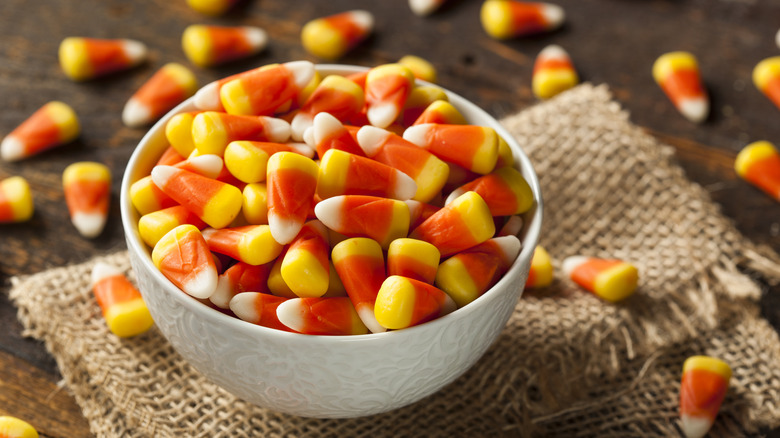 A bowl of candy corn with bits of candy corn scattered around.