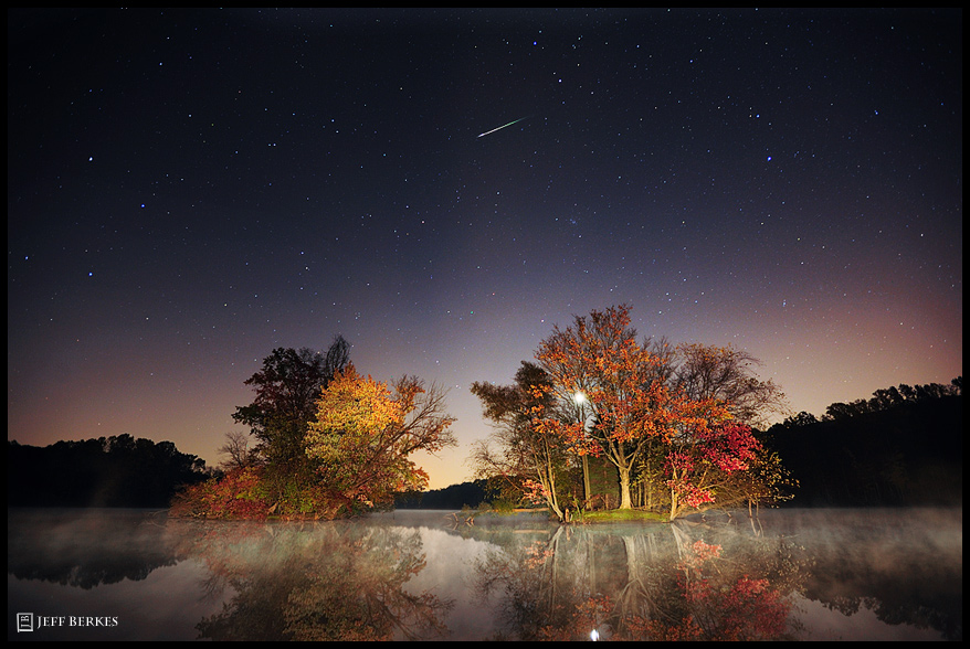 Meteor streaking across the sky above a lake and several trees.