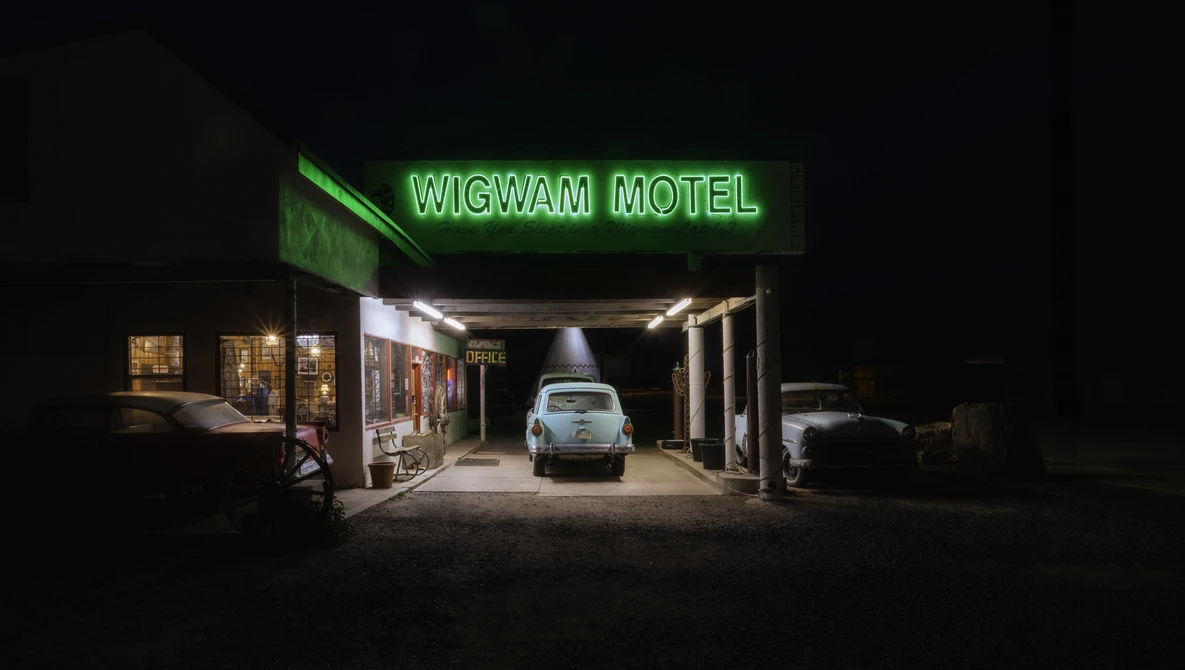 Wigwam Motel storefront at night with neon green sign and parked vintage car