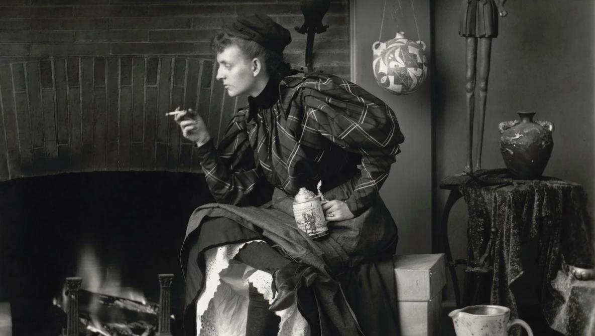Woman in dark clothing sits by fireplace in vintage interior setting