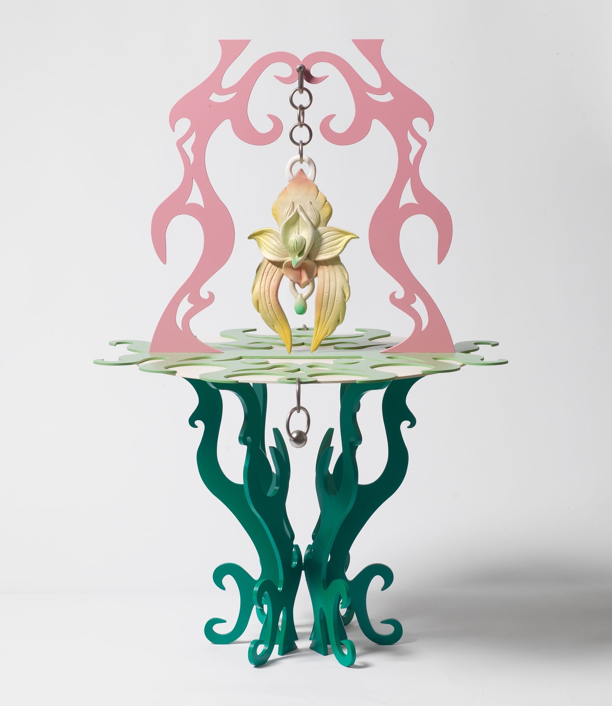 a colorful, carved sculpture of a table-like structure with an orchid dangling from a chain