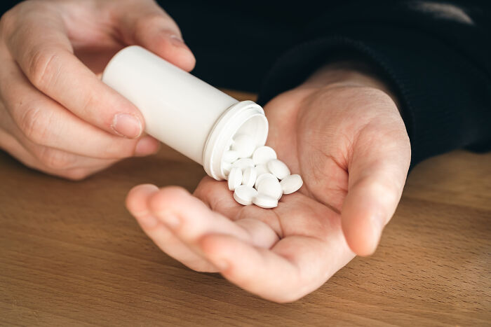 Close-up of a person pouring white pills into their hand, reflecting experiences of people feeling sick.