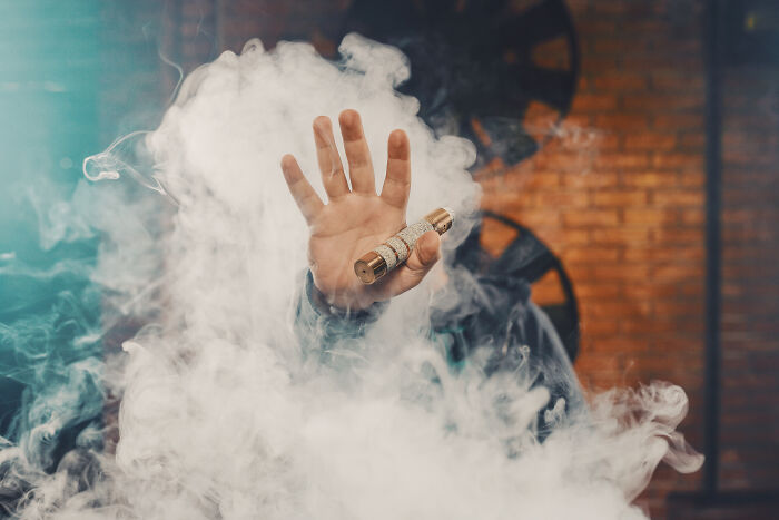 Close-up of a hand holding a vape pen surrounded by thick smoke, highlighting health risks in Gen Z.