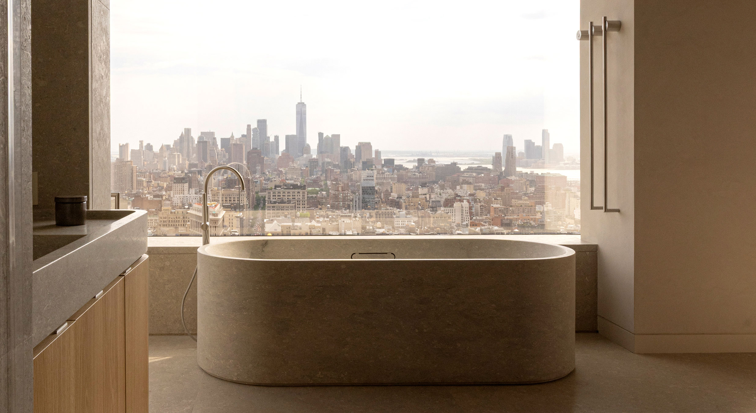 Stone bathtub in the principal bathroom at 262 Fifth Avenue, positioned in front of floor-to-ceiling glazing with panoramic views across Lower Manhattan.