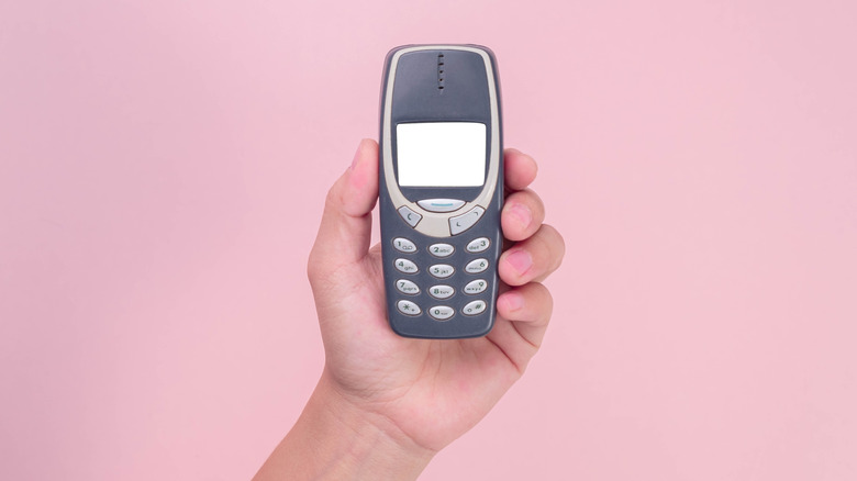 Hand holding a Nokia 3310 cell phone against a pink background.