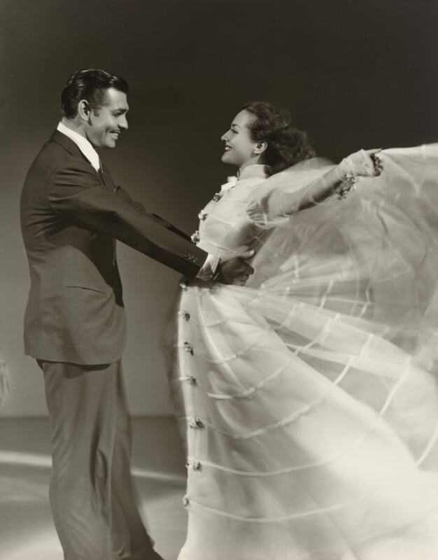 Clark Gable and Joan Crawford dance together, with Crawford wearing a flowing white gown that billows out to the side.