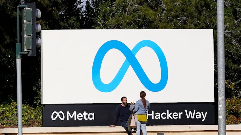 People talk near a Meta sign outside of the company's headquarters in Menlo Park.