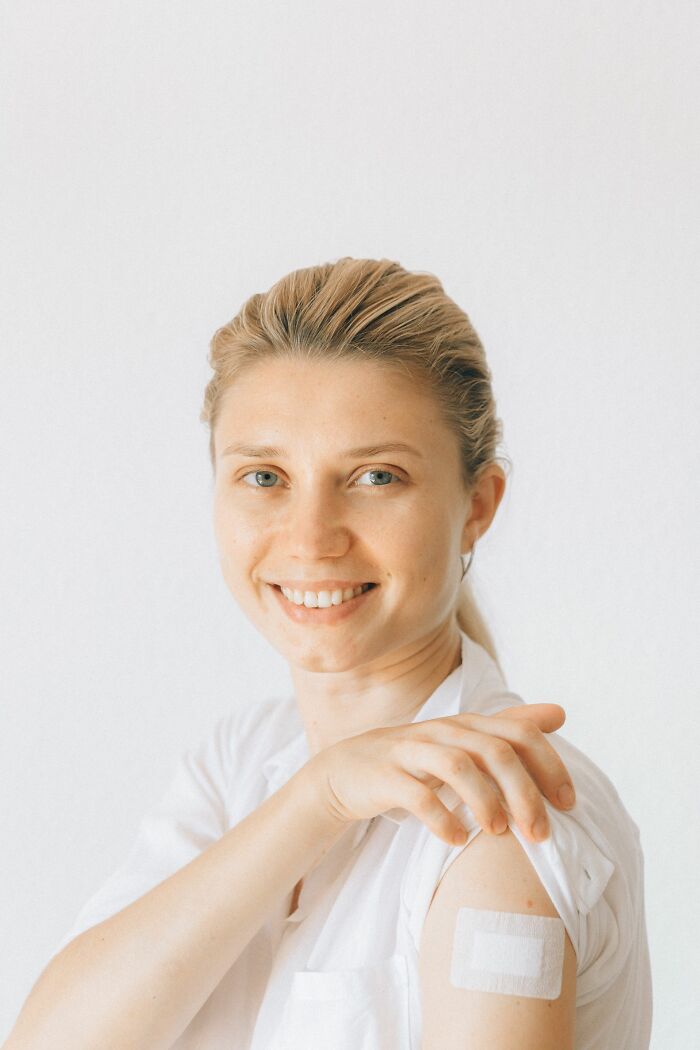 A smiling woman showing a bandage on her arm after a vaccination, relevant to doctors and nurses.