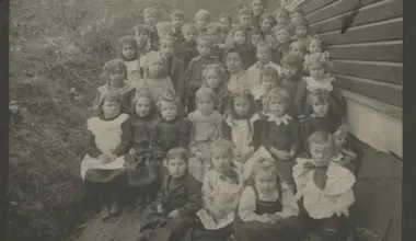 Large group portrait of approximately 40 children arranged in rows outside a building