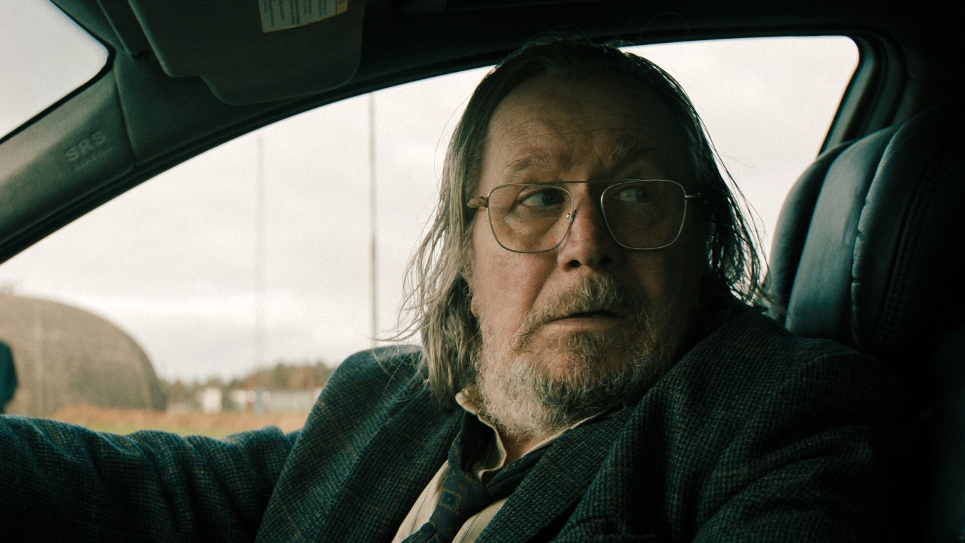 Sir Gary Oldman sitting in a car looking nervous in a production still from Slow Horses.