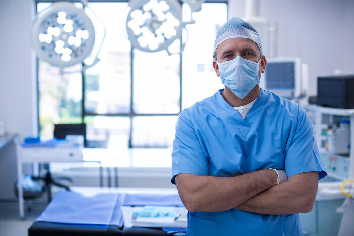 A surgeon wearing blue scrubs and a face mask in an operating room representing medical doctors.