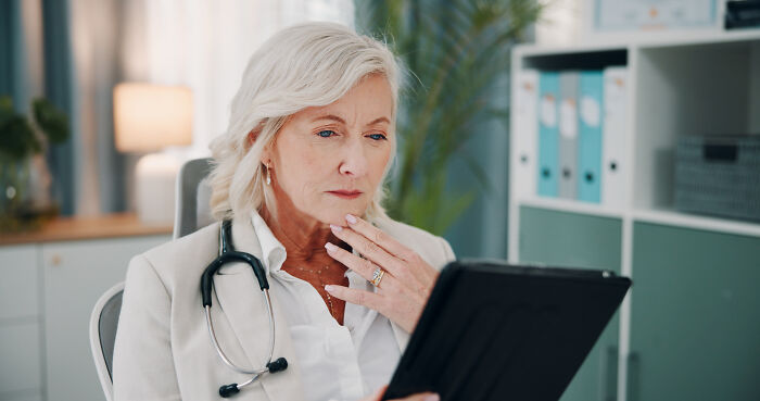 An experienced female doctor with a stethoscope examining a digital tablet.