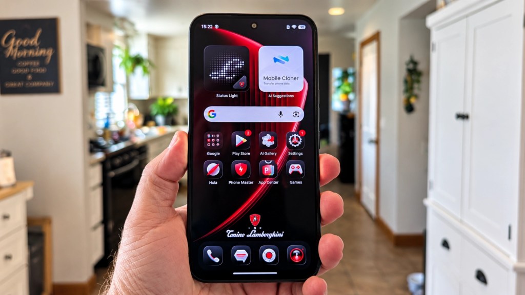 A person holding a smartphone displaying a home screen with various app icons, including Google, Gallery, and Settings, set against a kitchen background.