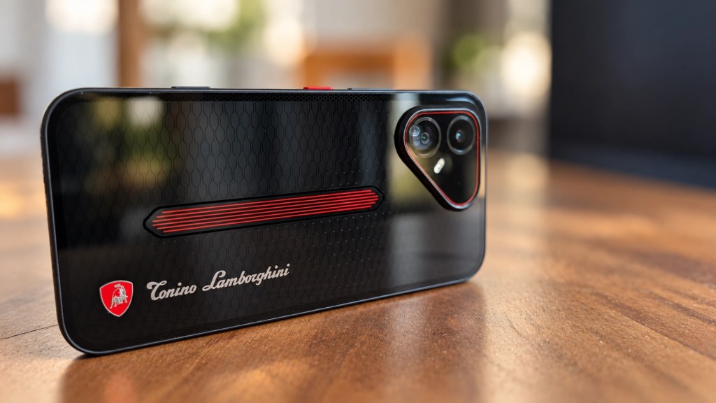 A close-up of a black smartphone with a honeycomb pattern, featuring red accents and the logo of Tonino Lamborghini on the back, resting on a wooden surface.
