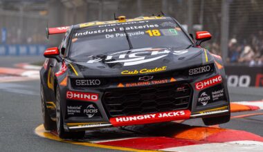 Black and gold Supercar number 18 bounces over a curb at a street circuit.