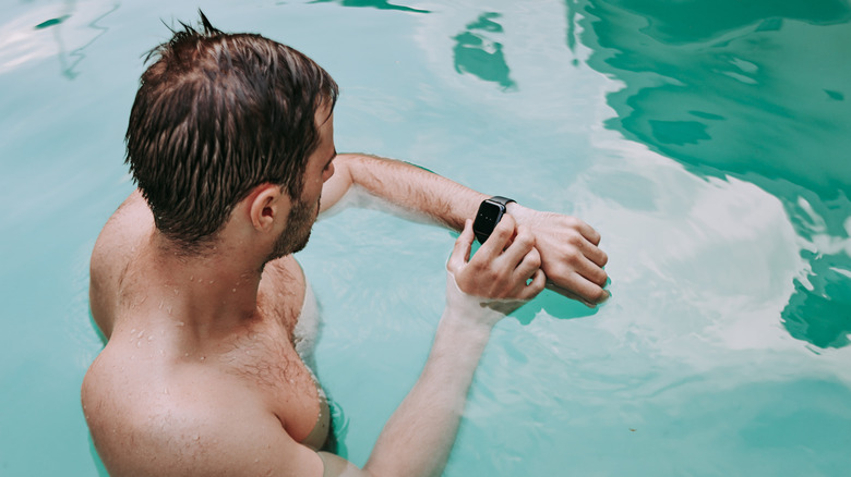 A person checking a smartwatch attached to his wrist while inside a pool