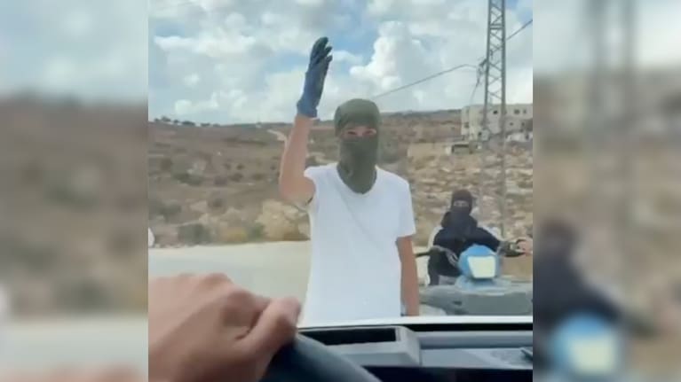 In this image made from video provided by Amit Orfali, masked Israeli settlers confront a car driven by Israeli activists in the West Bank village of Taybeh.