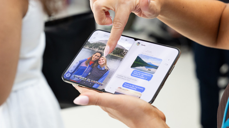 Finger pointing at the inner screen of Apple's iPhone Duo, showing messages and a full-screen photo.