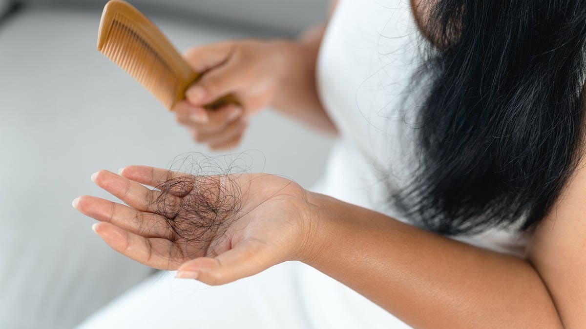 woman holding a comb with loose hair strands visible.