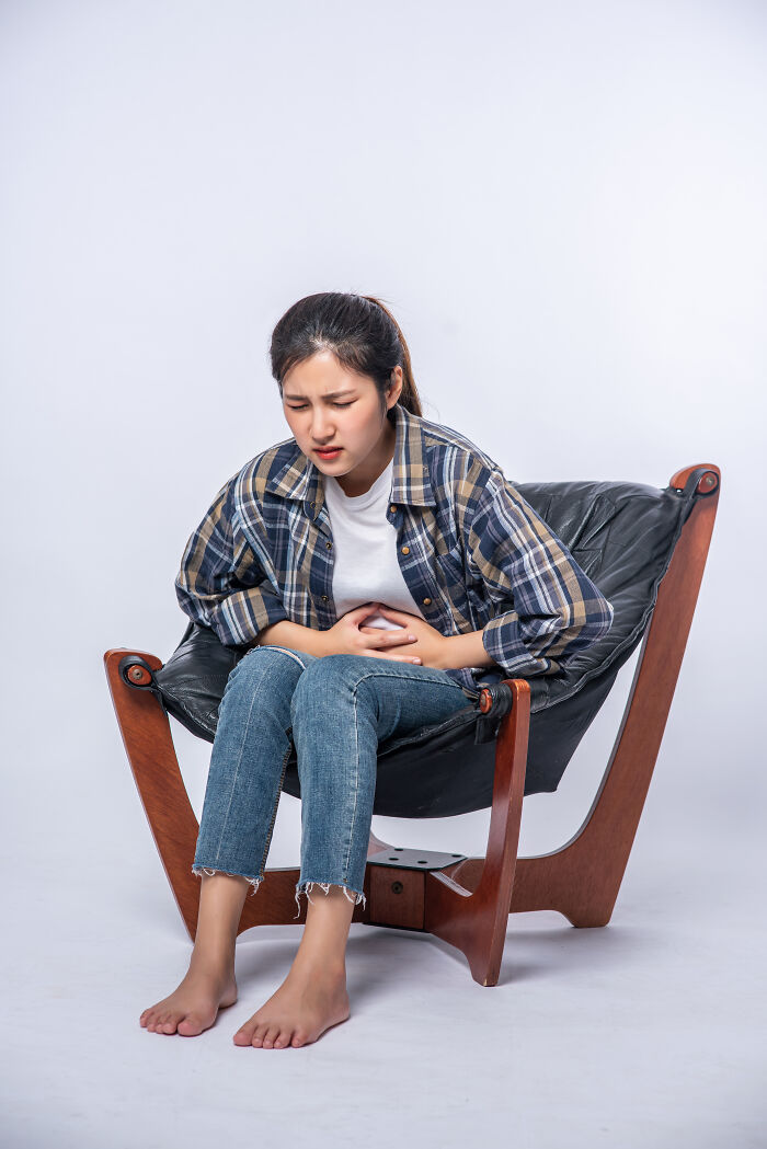 A young woman sitting in a chair holding her stomach, showing signs of Gen Z health problems.