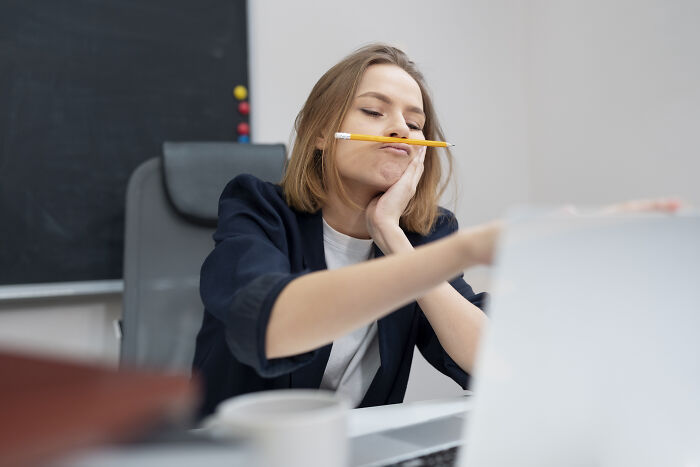 A bored or fatigued young woman at her desk with a pencil under her nose, symbolizing health problems in Gen Z.
