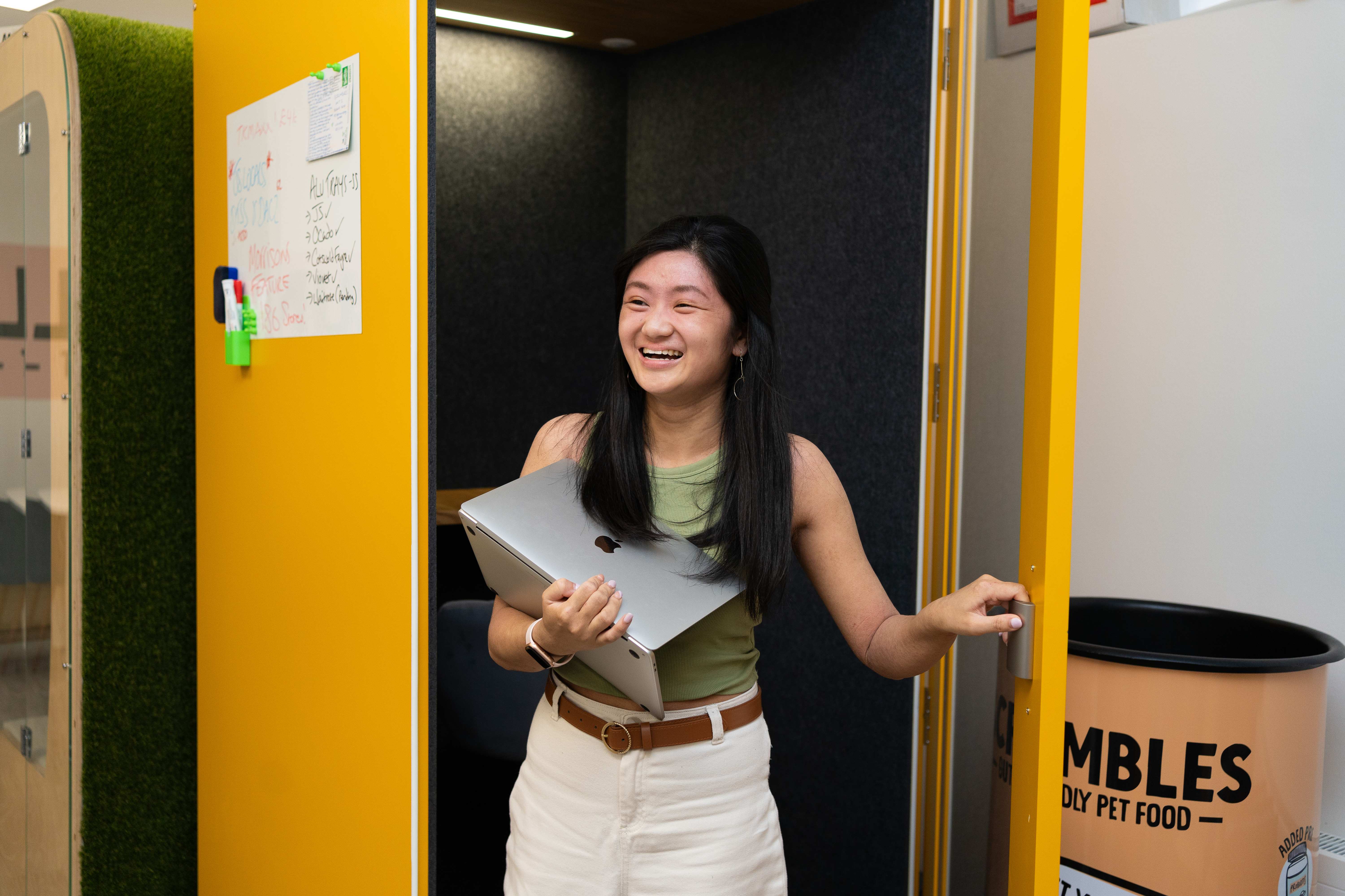 Woman leaving a yellow office pod with a laptop.