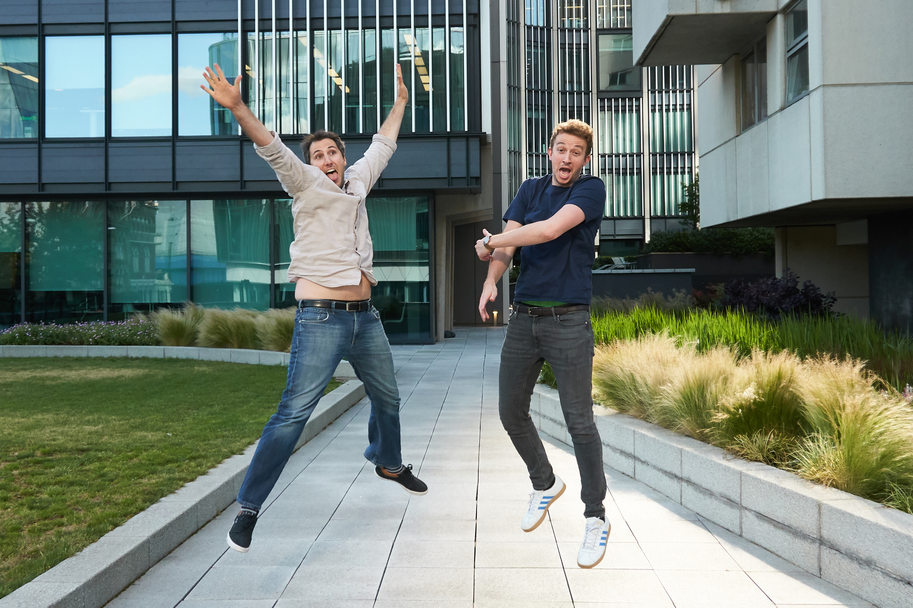 Two men joyfully jumping in front of a modern building.