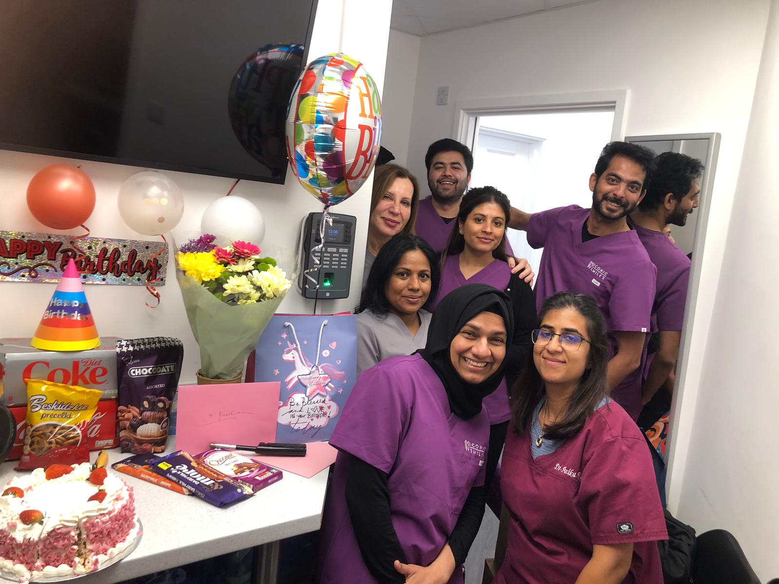 Team celebrating a birthday with cake and gifts.