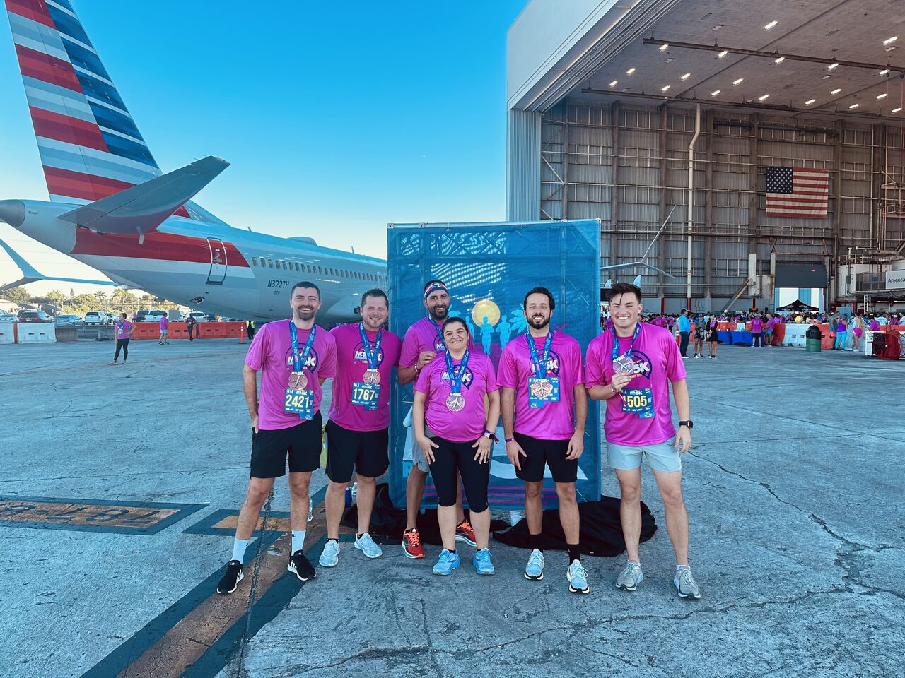 Group of six people in pink shirts and medals after a race.
