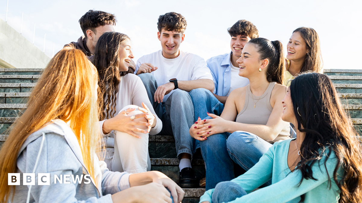 Eight young people sitting on steps outside on what looks a sunny day. Three are male and five are female