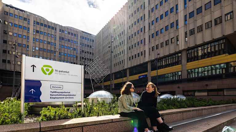 People sitting outside a building next to a TE services sign.