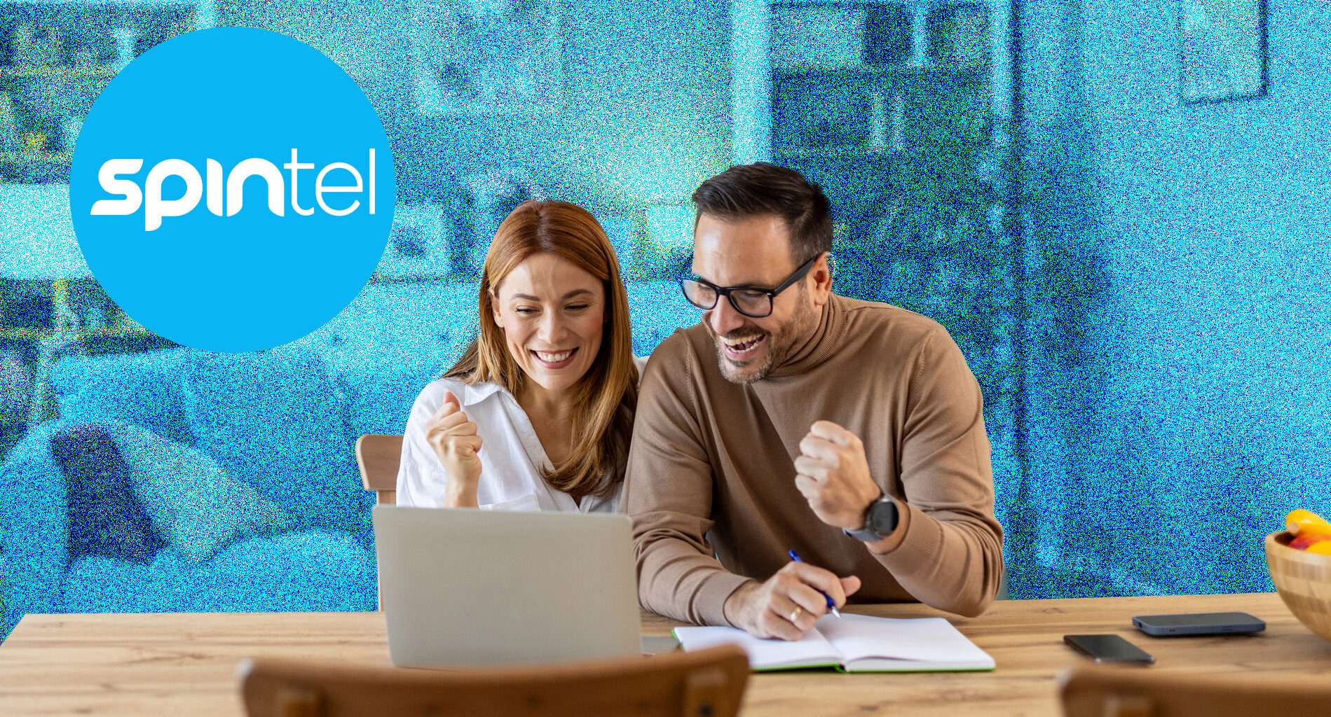A young couple sitting at a table and cheering while looking at a laptop. The background is blue and the SpinTel logo is in the top left.
