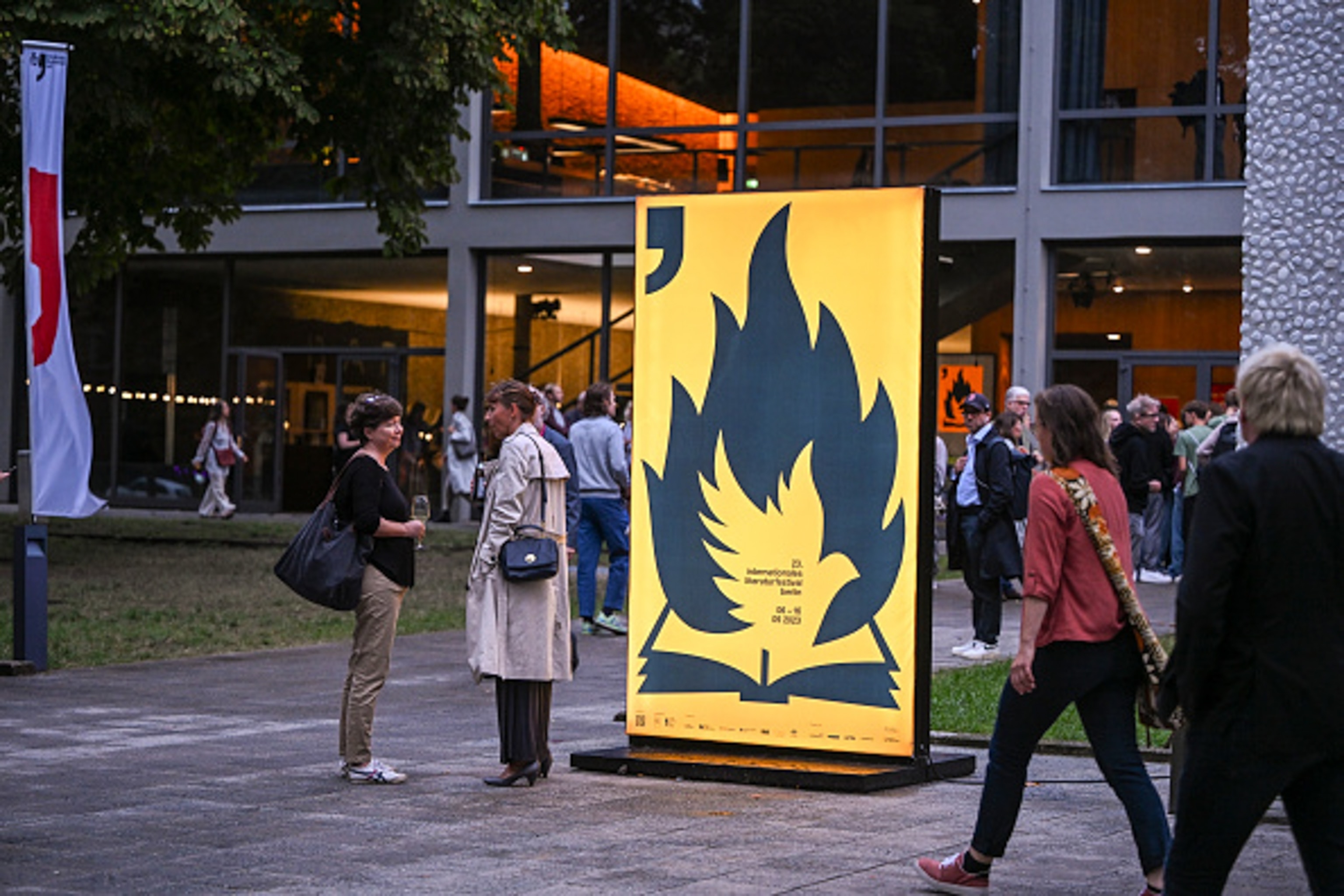 A lager yellow sign with a book as people walk into the building.