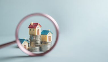 A magnifying glass is placed over three small toy houses sitting on piles of coins