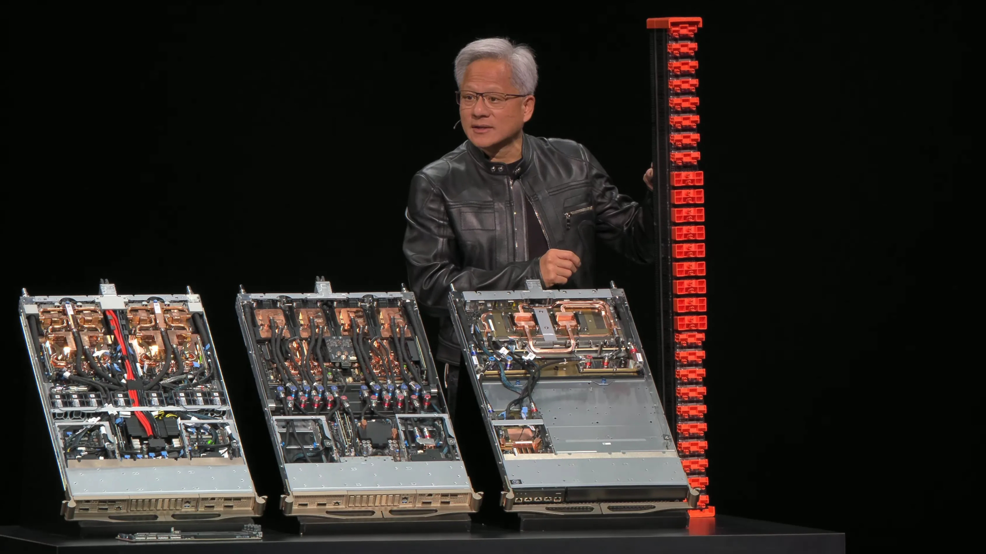 An image of the live presentation broadcast by Nvidia at Computex 2025, where CEO Jen-Hsun Huang holds an NVLink Fusion spine next to three Nvidia rank units.