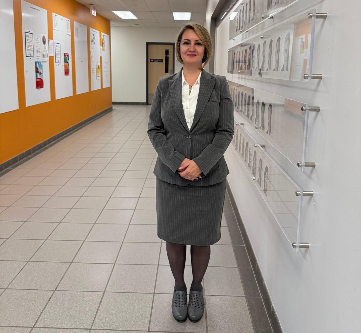 A woman in a grey skirt suit stands in a hallway.