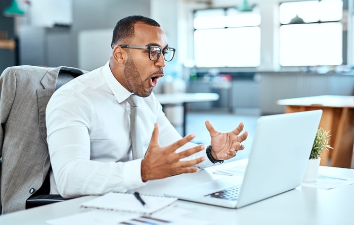An excited and happy middle-aged man sitting at a desk looking at a laptop screen.