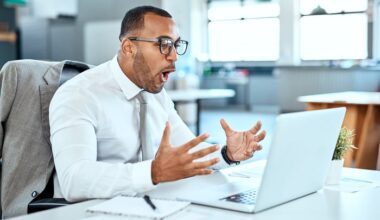An excited and happy middle-aged man sitting at a desk looking at a laptop screen.