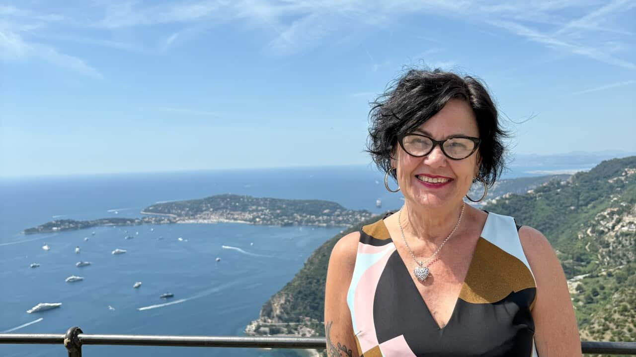 A smiling, middle-aged woman posing atop a hill with views of a waterway in the background.