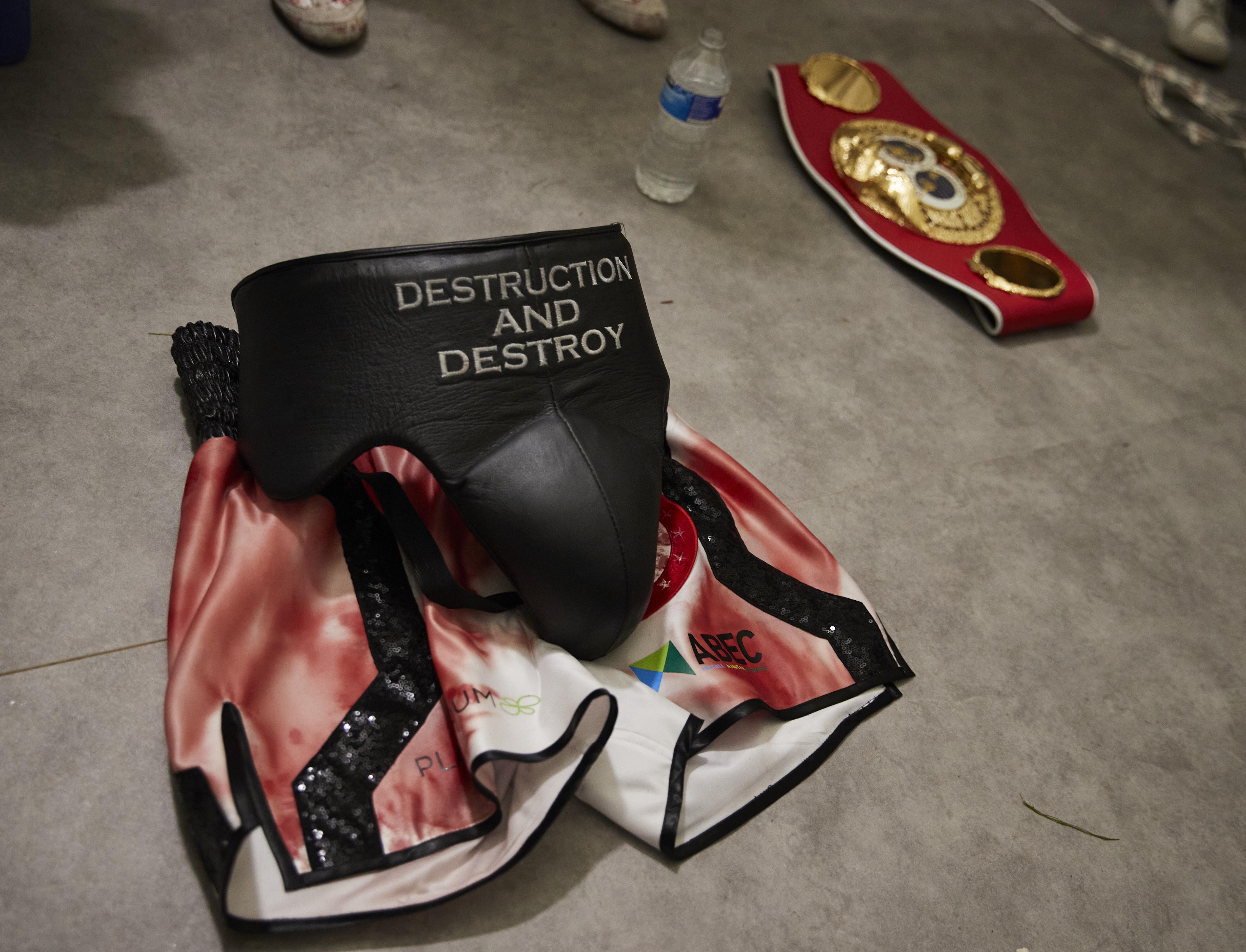 Bloody boxing shorts, groin protector, and IBF world championship belt on the floor.